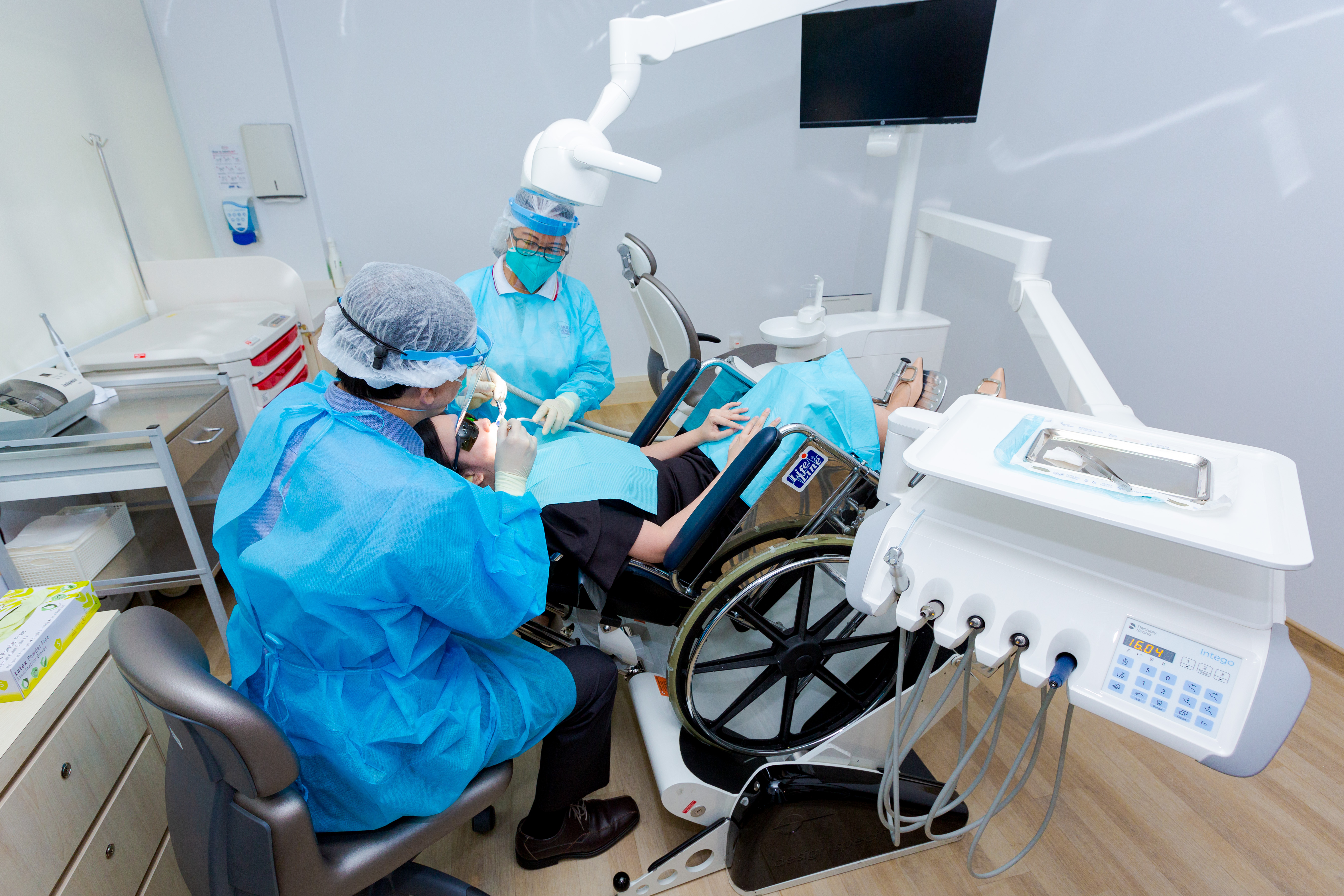 A wheelchair user undergoing a dental procedure with a dentist and a nurse in a dental clinic.
