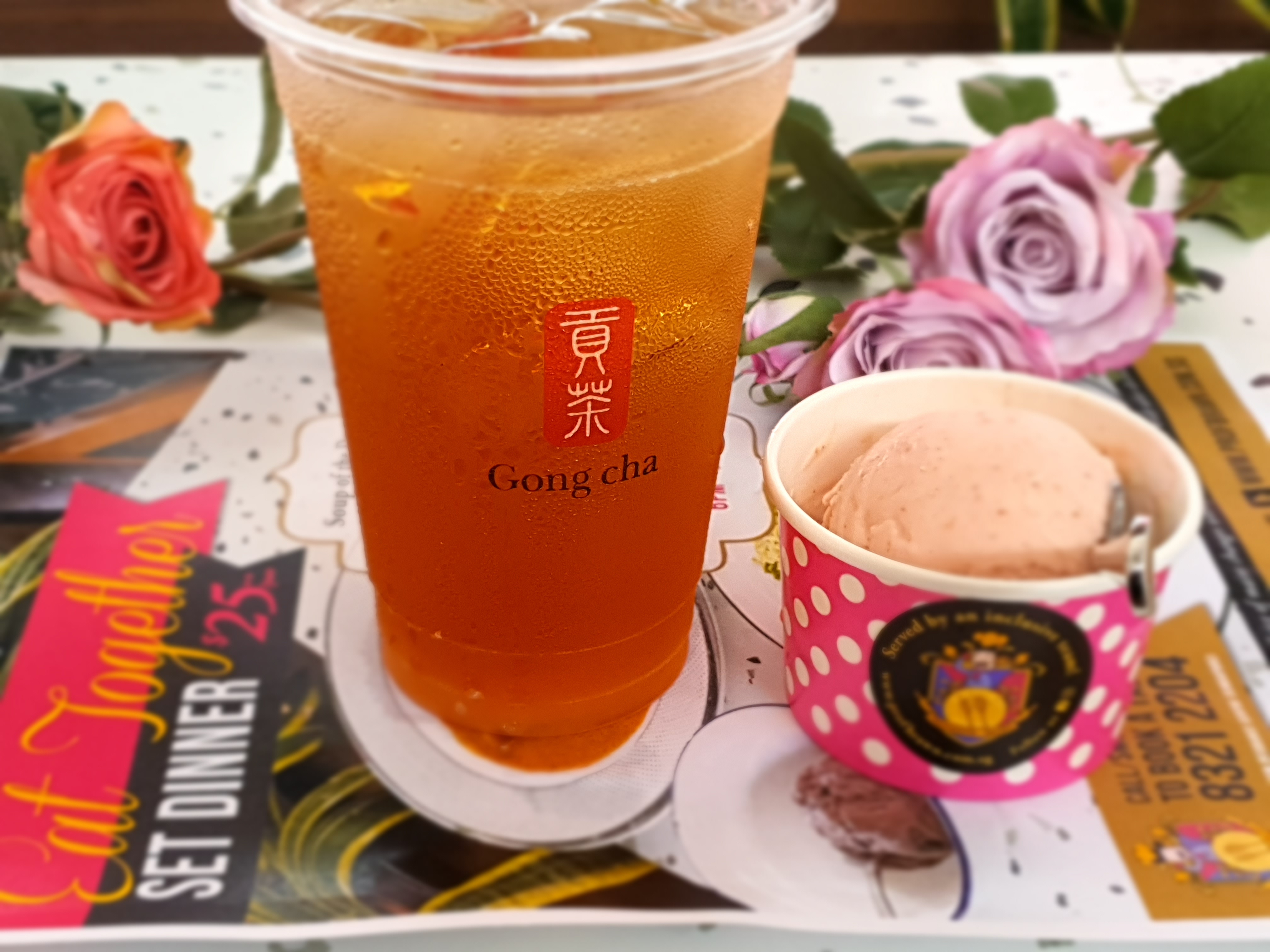 A cup of Gong Cha tea, and ice-cream on a table with floral decorations in the background.